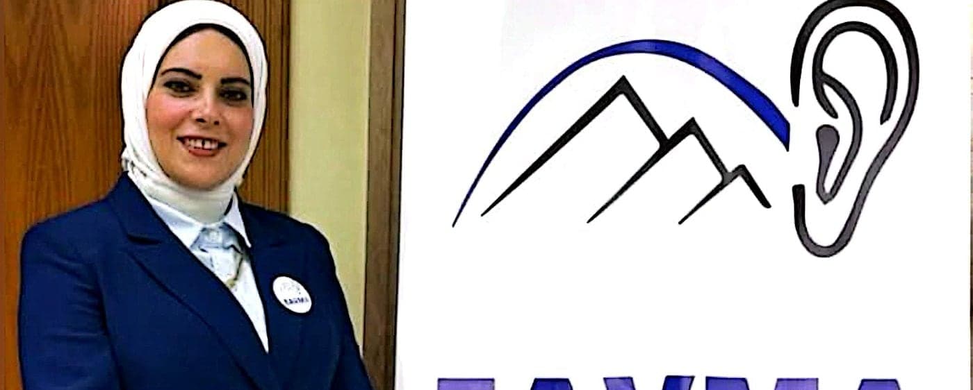 د. فاطمة رجب أمام شعار الجمعية المصرية لطب السمع والاتزان